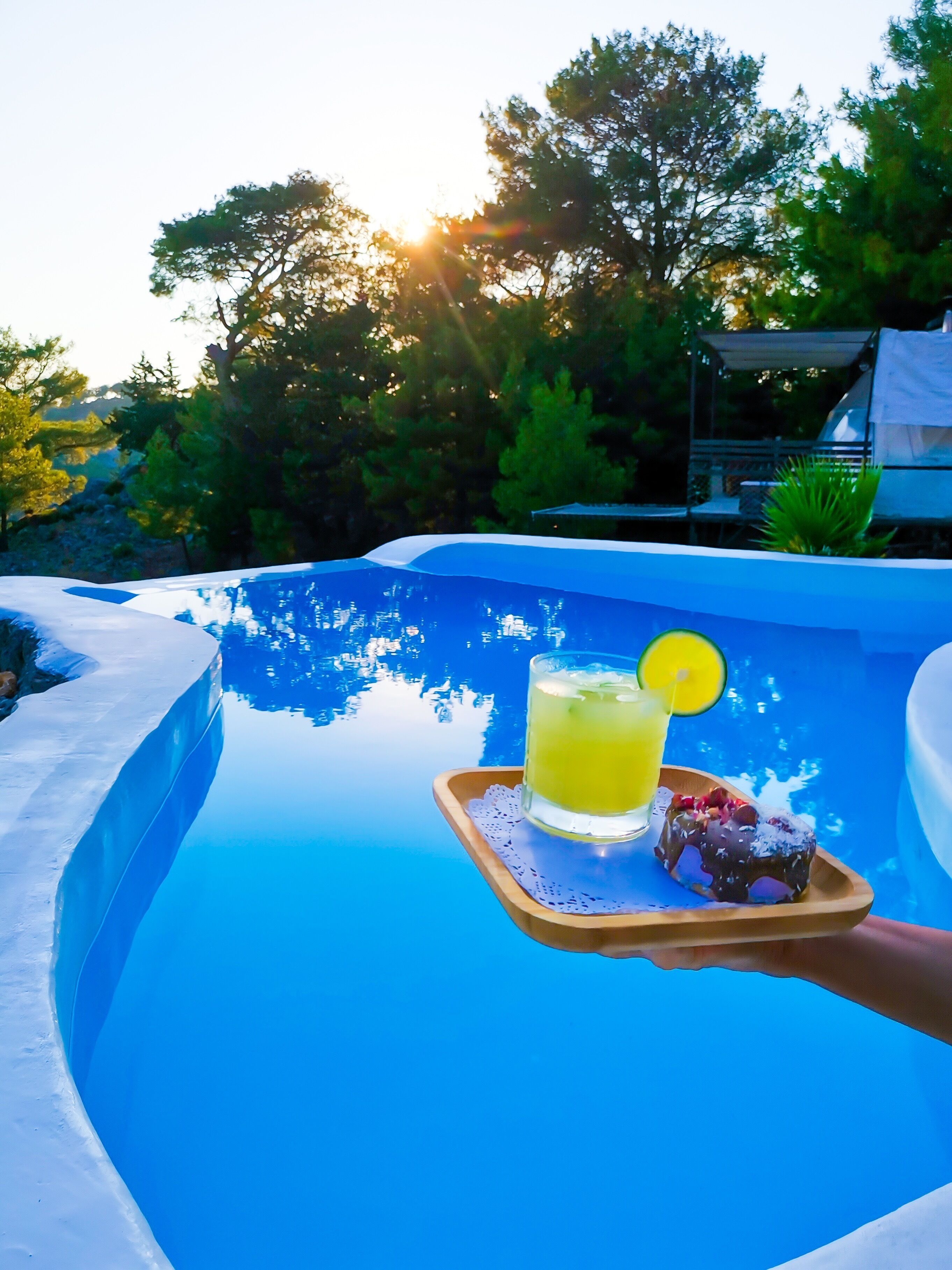A poolside setting with a drink and dessert on a tray.