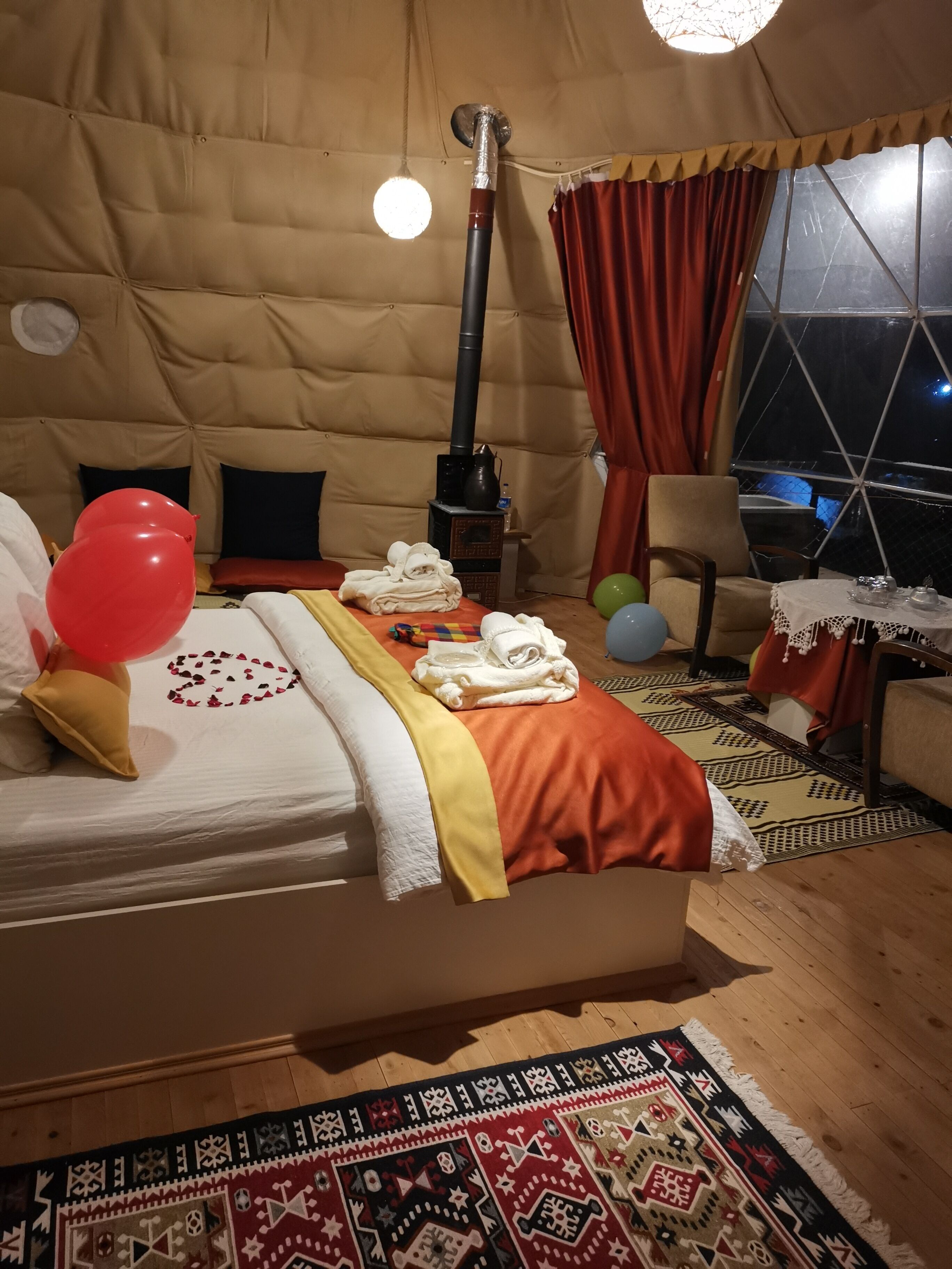 A cozy room with a bed, a table with a lamp, a window, and a fireplace.