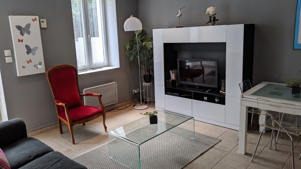A modern living room with a red chair, a glass coffee table, a fireplace, and a dining area with a table and chairs. - Apartment Biarritz - Quartier Saint Martin (Biarritz)