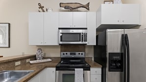 A kitchen with white cabinets, a stainless steel refrigerator, a microwave, and an oven.