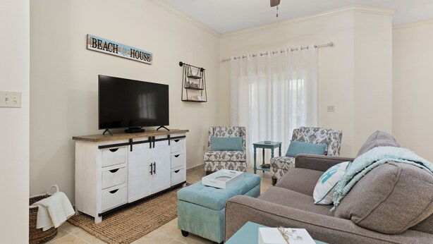 A living room with a television, a sofa, a patterned armchair, and a ceiling fan.