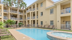 A multi-story hotel with a swimming pool, outdoor seating, and palm trees.