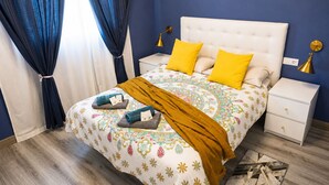 Une chambre à coucher comprenant un lit, deux tables de chevet, une commode, une fenêtre avec des rideaux et une couvre-lit à motifs.