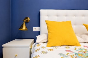 Een slaapkamer met een wit bed, een geel kussen, een witte nachtkastje en een gouden lamp.
