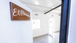Un couloir avec une enseigne en bois sur laquelle on peut lire « El Miramar », un mur blanc et une porte donnant sur une autre pièce.