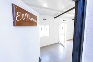 A hallway with a wooden sign reading 'El Miramar,' a white wall, and a door leading to another room. - - (Buenavista del Norte)