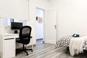 A bedroom with a bed, a desk with a computer, and a chair.