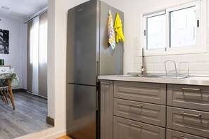 A modern kitchen with a stainless steel refrigerator, grey cabinetry, and a window with blinds.