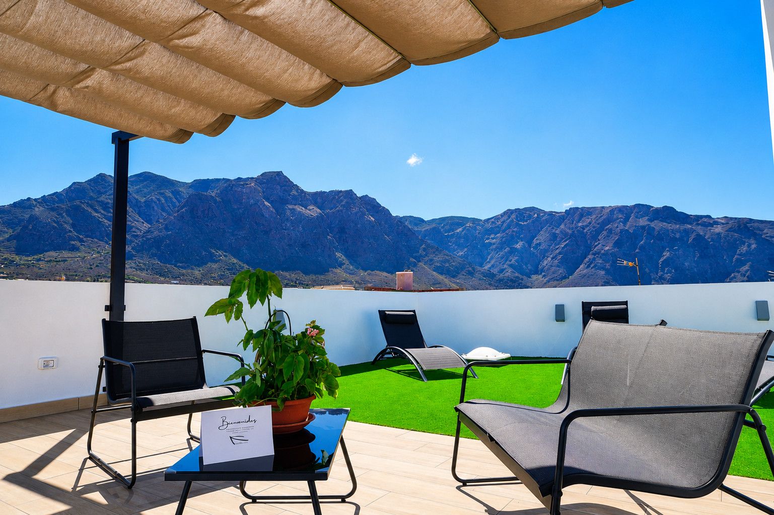 Eine Terrasse mit Blick auf Berge, ein Tisch mit einer Pflanze und zwei Stühle.
