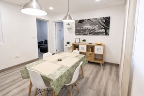 Ein Essbereich mit einem Tisch für vier Personen, zwei Pendelleuchten, einem an der Wand befestigten Regal mit Dekorationen und einem gerahmten Bild.