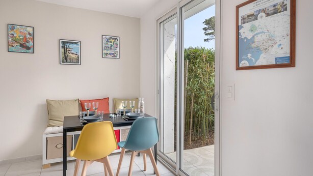 Un coin repas avec une table dressée pour deux personnes, un canapé et une grande fenêtre donnant sur un jardin de bambous.