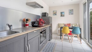 Une cuisine moderne avec un évier en acier inoxydable, une machine à café rouge et un four à micro-ondes. On y trouve également un coin repas avec une table et des chaises colorées.