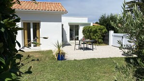 Une maison moderne avec un toit en tuiles, une terrasse avec une table et des chaises, et une pelouse bien entretenue.