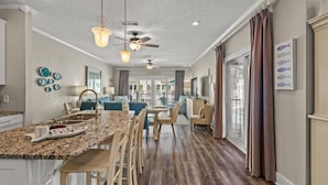 A spacious kitchen with a granite countertop, bar stools, and a dining area with a large window. - Beachside Townhome w/ Pool |5 Decks | prime spot (Mexico Beach)
