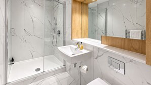 A modern bathroom with a glass-enclosed shower, a white sink, and a wooden vanity. - Luxurious ONE Bedroom Apartment IN Bond Street (Chelmsford)