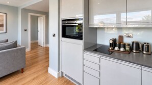 A modern kitchen with white cabinetry, a built-in oven, and a countertop with a coffee maker, kettle, and cups. - Luxurious ONE Bedroom Apartment IN Bond Street (Chelmsford)