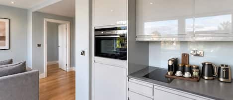 A modern kitchen with white cabinetry, a built-in oven, and a countertop with a coffee maker, kettle, and cups.