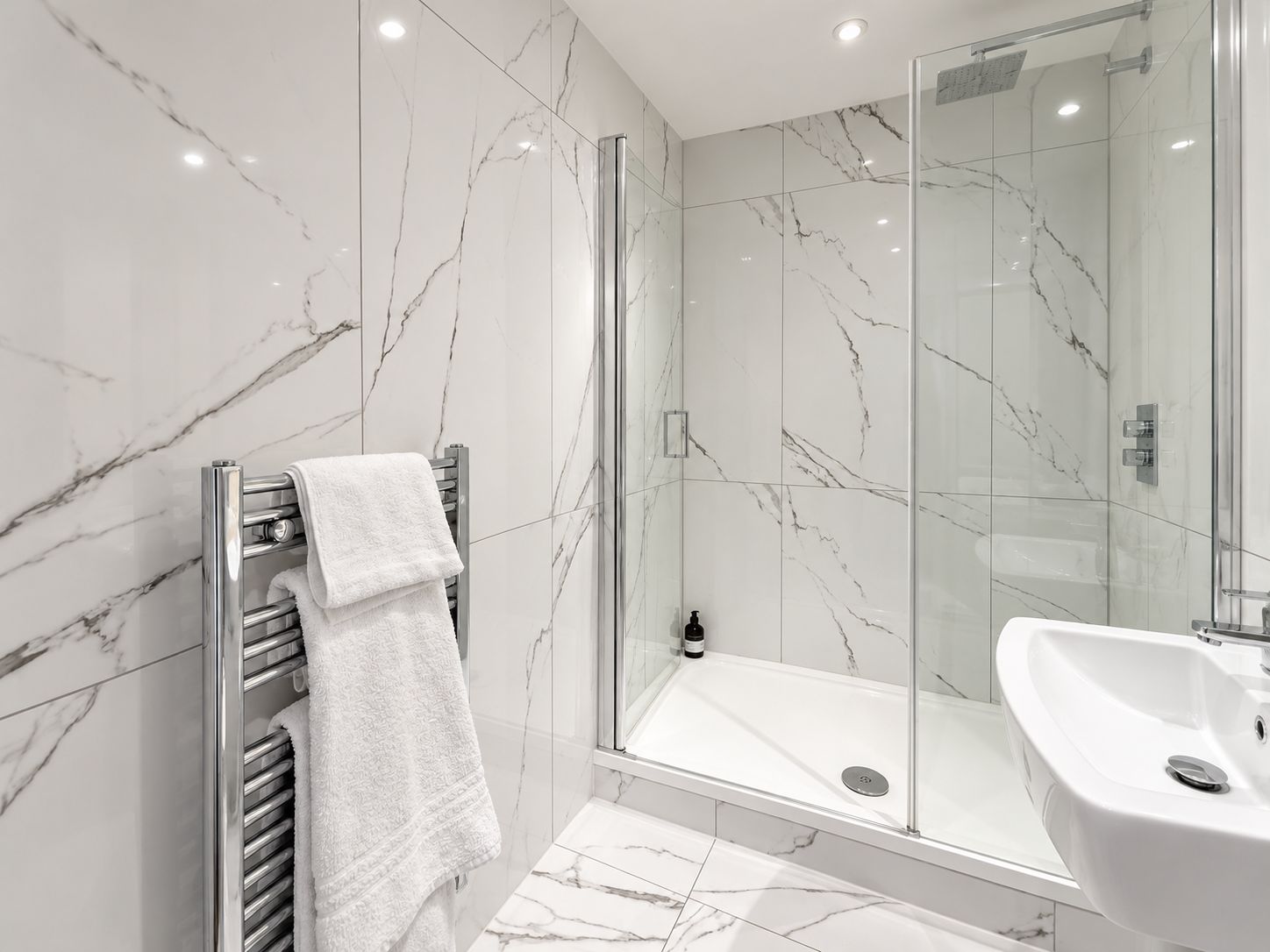 Une salle de bain moderne avec une douche à parois de verre, un lavabo encastré et un porte-serviettes sur lequel est posée une serviette pliée.