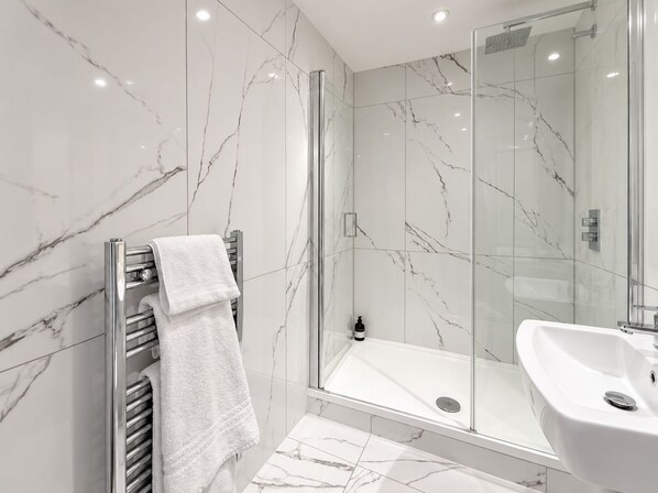 Un baño moderno con cabina de ducha de vidrio, lavamanos integrado y toallero con una toalla doblada.