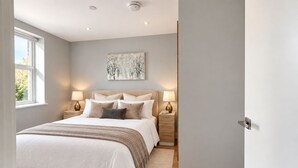 A bedroom with a large bed, bedside lamps, a nightstand, and a window. - Luxurious ONE Bedroom Apartment IN Bond Street (Chelmsford)