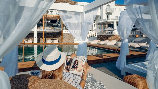A poolside area with a view of a building, white canopies, and lounge chairs. - Penelope Village Mykonos by Mr and Mrs White (Mykonos)