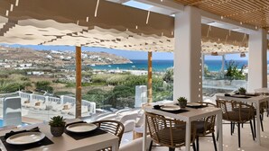 A restaurant with outdoor seating overlooking a coastal view, featuring white furniture and a wooden ceiling. - Penelope Village Mykonos by Mr and Mrs White (Mykonos)