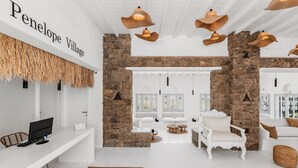 A spacious room with a stone wall, white furniture, and a desk with a computer. - Penelope Village Mykonos by Mr and Mrs White (Mykonos)