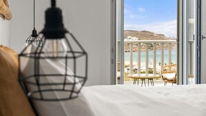 A bedroom with a bed, a hanging light fixture, and a balcony with a view of the sea and hills. - Penelope Village Mykonos by Mr and Mrs White (Mykonos)