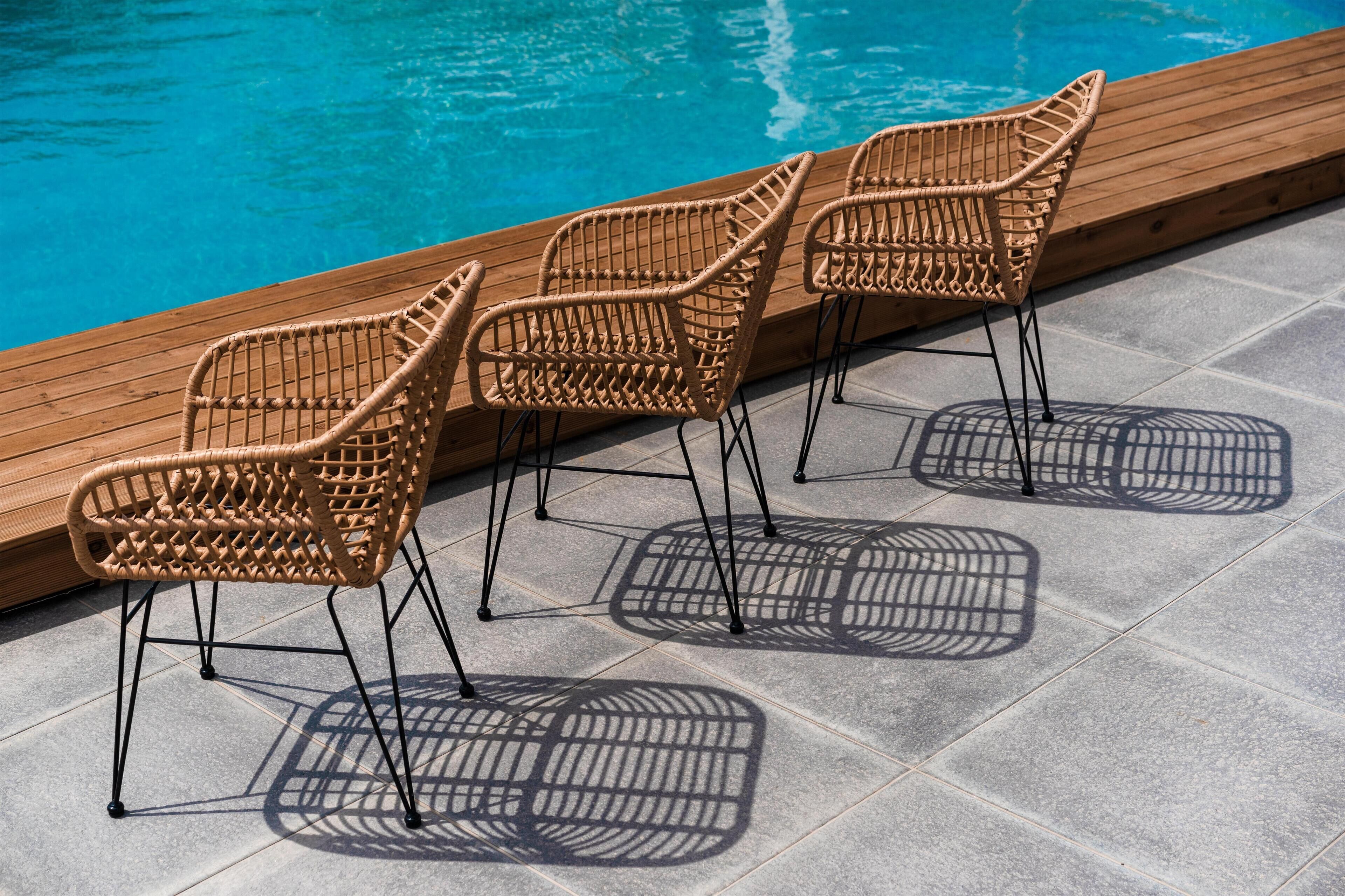 Tre sedie in vimini con gambe in metallo accanto a una piscina.