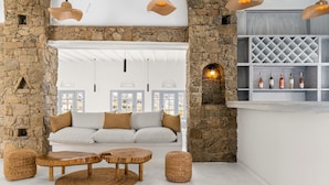 A cozy room with a stone wall, a white sofa, a wooden coffee table, and a wine rack with bottles. - Penelope Village Mykonos by Mr and Mrs White (Mykonos)