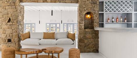 A cozy room with a stone wall, a white sofa, a wooden coffee table, and a wine rack with bottles.