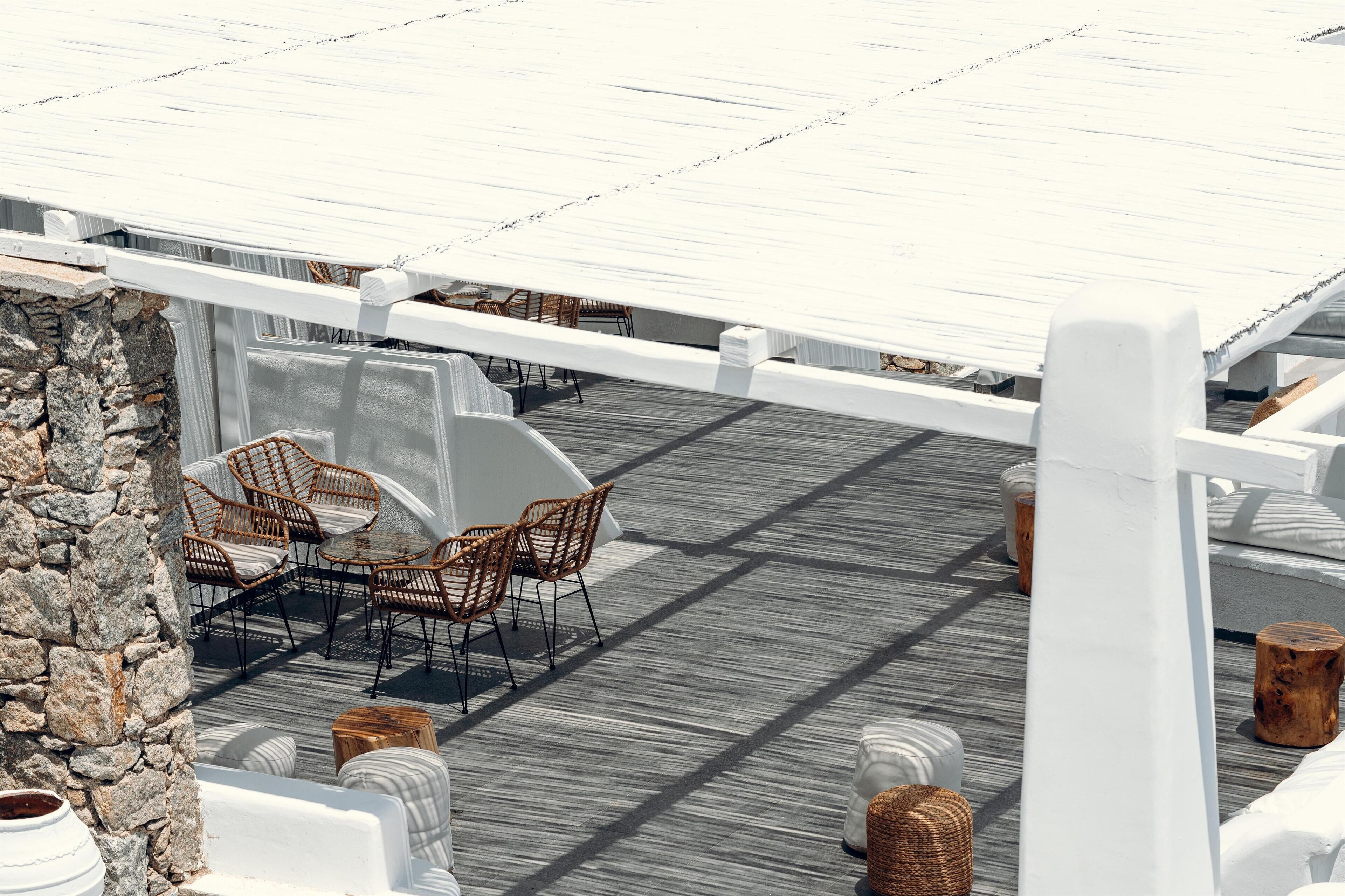 A rooftop terrace with wicker chairs and tables, stone walls, and a wooden deck.
