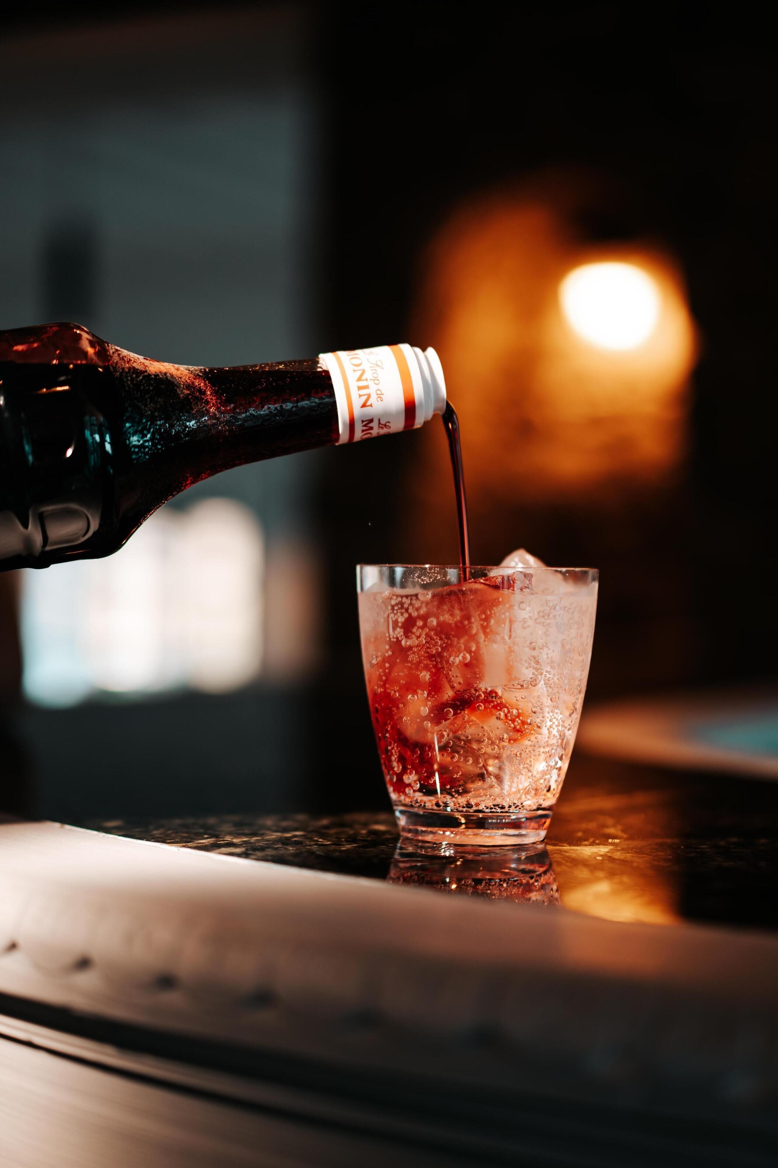 A bottle of Coca-Cola being poured into a glass with ice cubes.