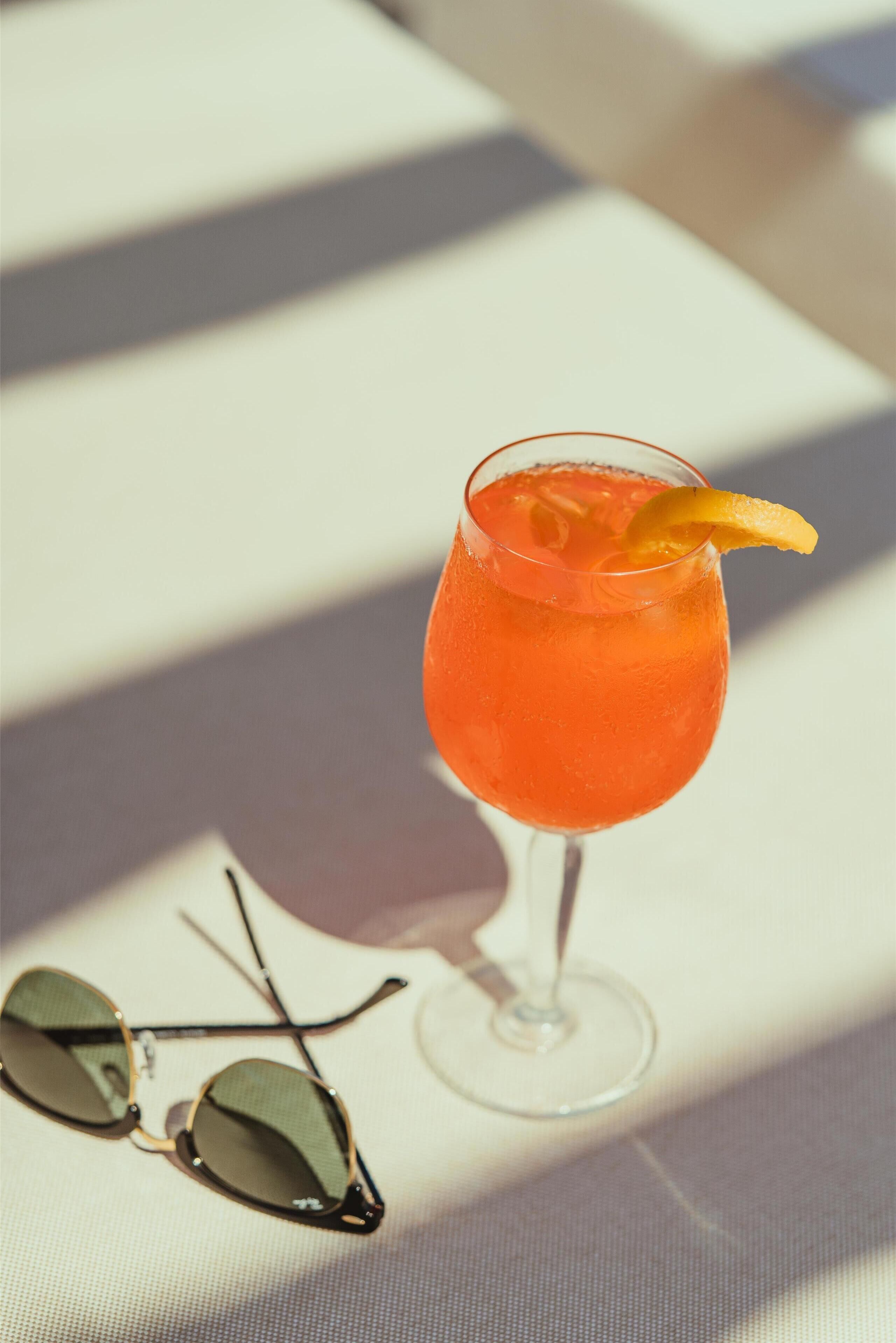 Un vaso de cóctel con una rodaja de naranja sobre una superficie blanca.