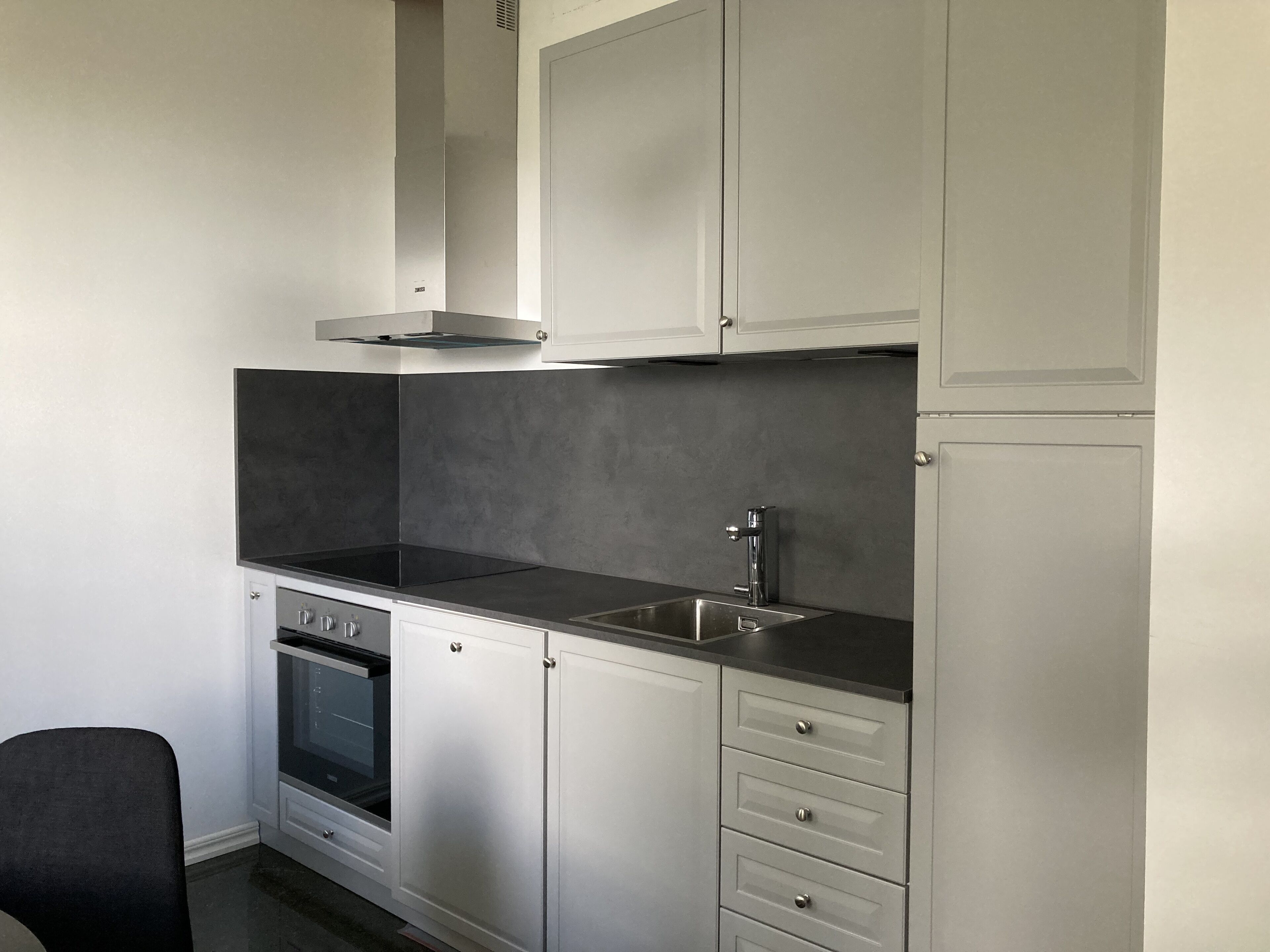 A compact kitchen with white cabinets, a black countertop, a stainless steel sink, and a built-in oven.