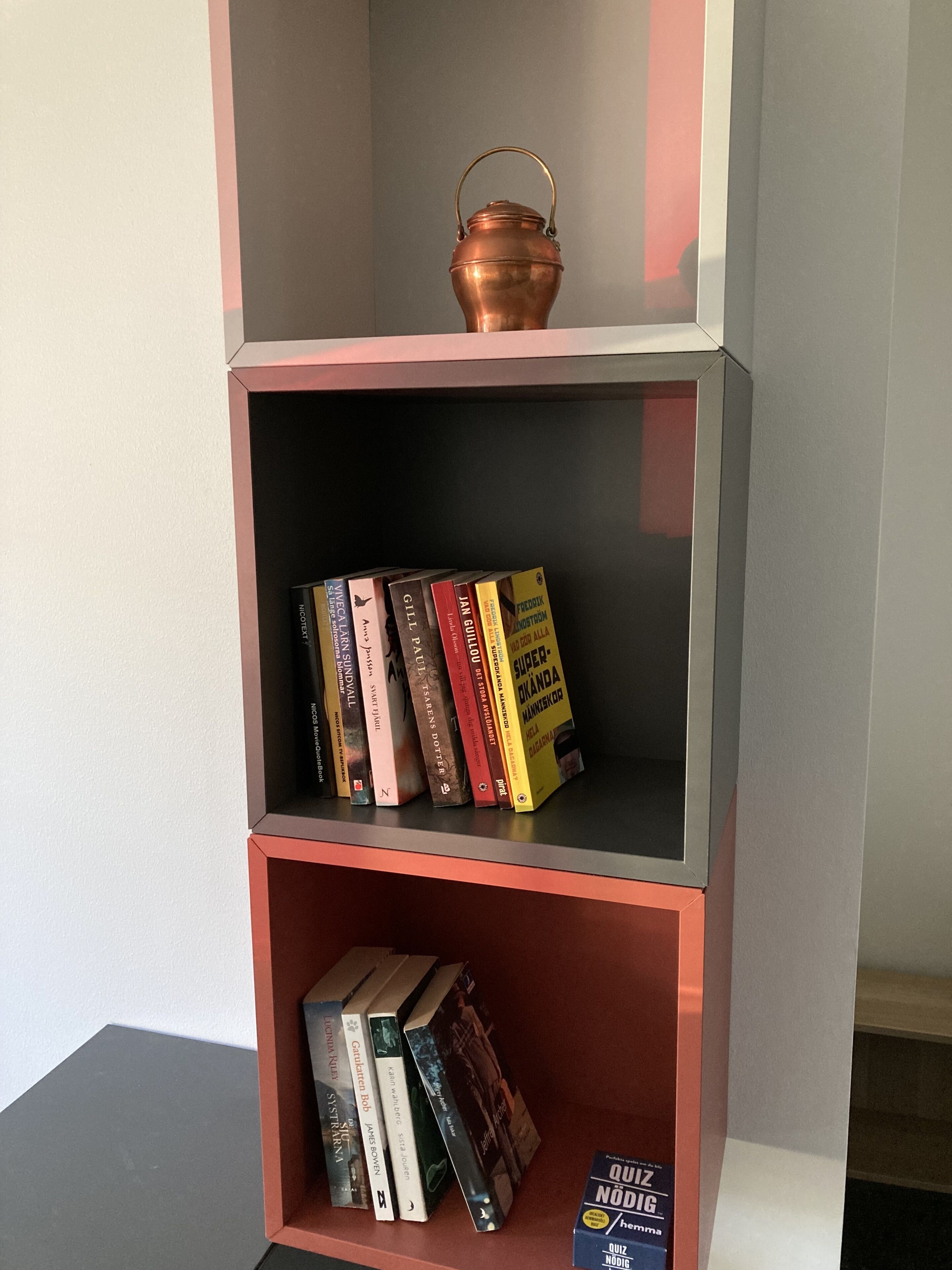 Una estantería con libros y una olla de cobre.