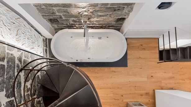 Un baño moderno con una bañera independiente, suelo de madera y pared de piedra.