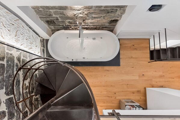 A modern bathroom with a freestanding bathtub, a wooden floor, and a stone wall. - Capitolare Tower (Portovenere)