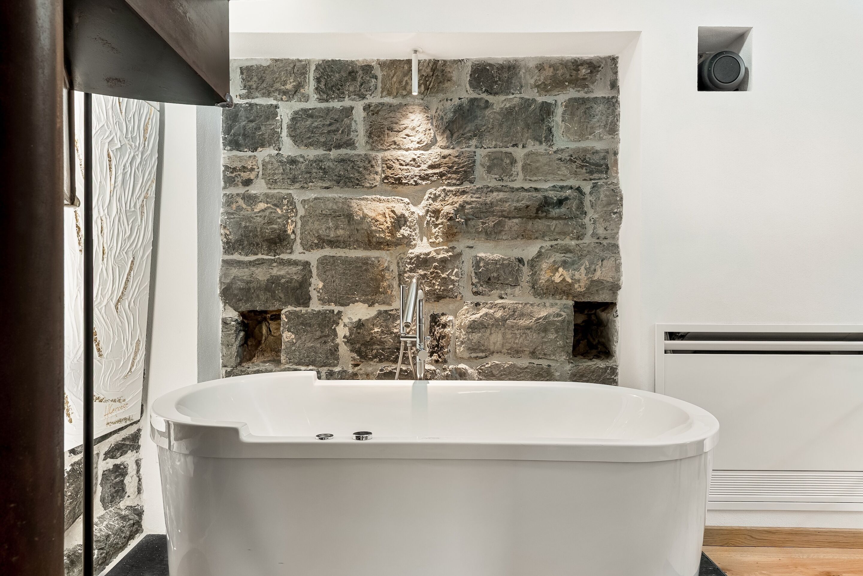 Een moderne badkamer met een vrijstaand bad, een stenen muur en een kleine speaker bevestigd aan de muur.