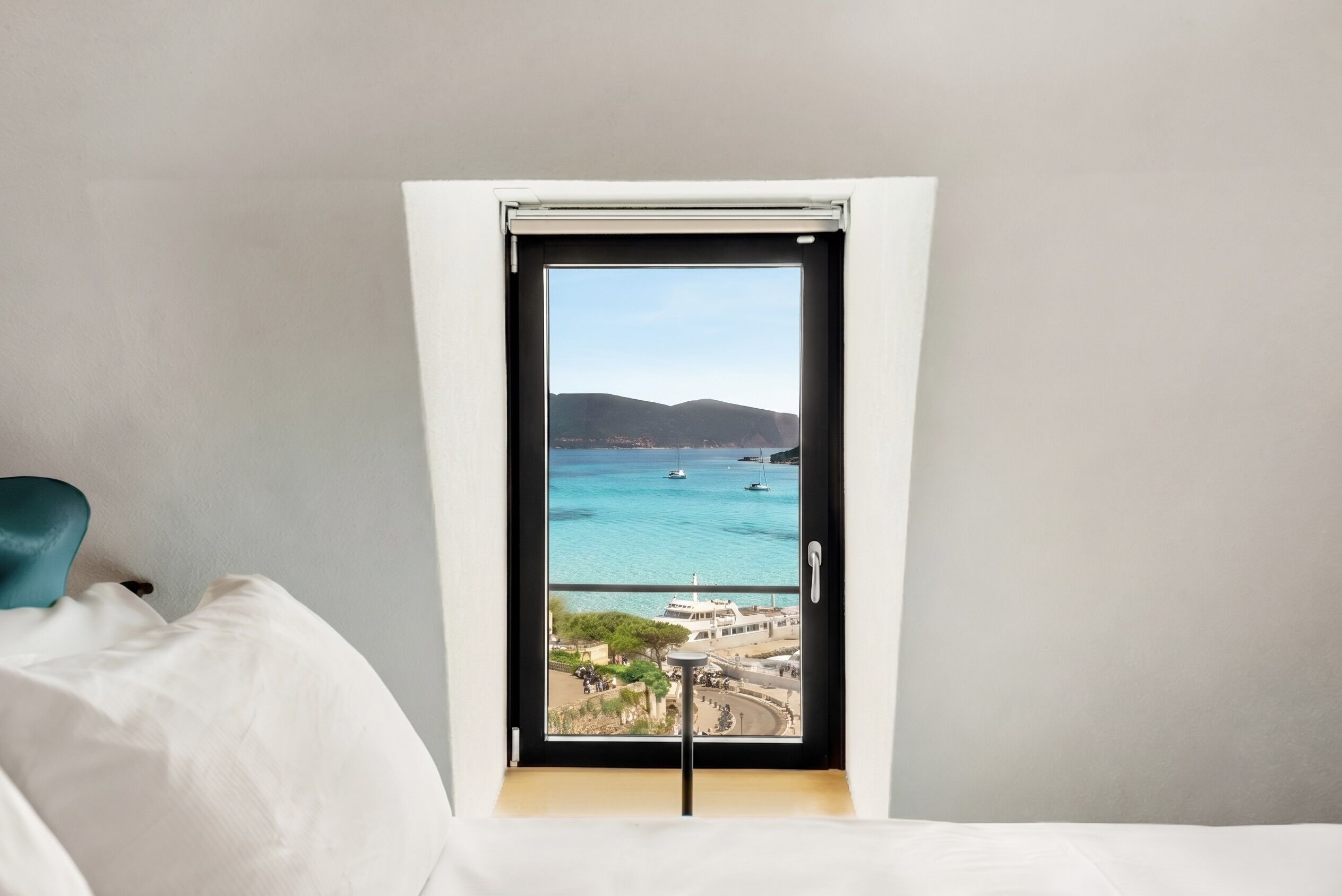 Una habitación con una cama, una ventana vista al mar y una silla.
