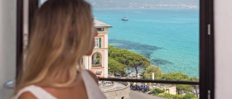 A woman overlooking a coastal town with a clear view of the sea and a sailboat.