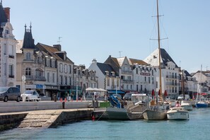 Un paseo marítimo con edificios históricos, un puerto deportivo con barcos y un camino peatonal.