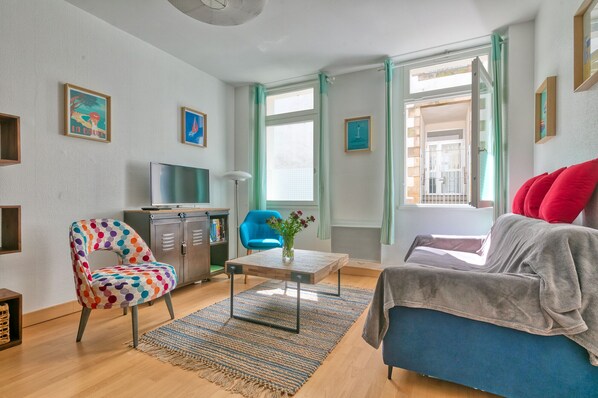 Una sala moderna con un sofá azul, un sillón colorido y un televisor sobre un mueble.