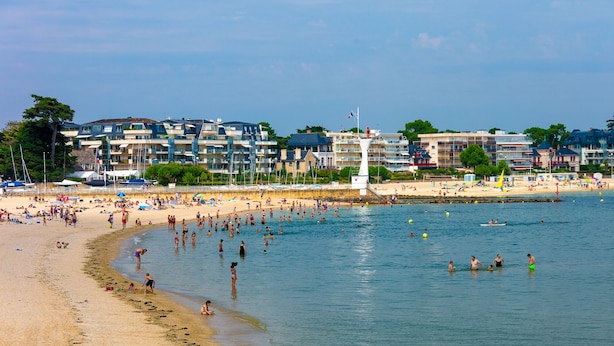 A beach with people swimming and sunbathing, a lighthouse, and buildings in the background. - Apartment Pouliguen Centre (Le Pouliguen)