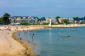 A beach with people swimming and sunbathing, a lighthouse, and buildings in the background. - Apartment in Downtown Pouliguen (Le Pouliguen)