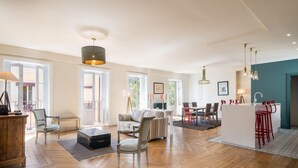 Un salon spacieux doté d’un parquet, d’un canapé, de fauteuils, d’une table basse et d’un coin bar avec des tabourets.