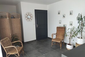 A room with a dark door, two wicker chairs, a potted plant, and wall-mounted pictures.