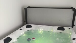 Ein Zimmer mit einer weißen Badewanne, gefüllt mit Wasser, einer schwarzen Kopfstütze und einem kleinen weißen Quadrat an der Wand.