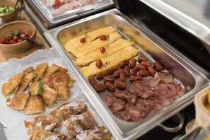 Un bufé con diversas opciones de comida, incluyendo pasteles, huevos, frijoles y tocino.