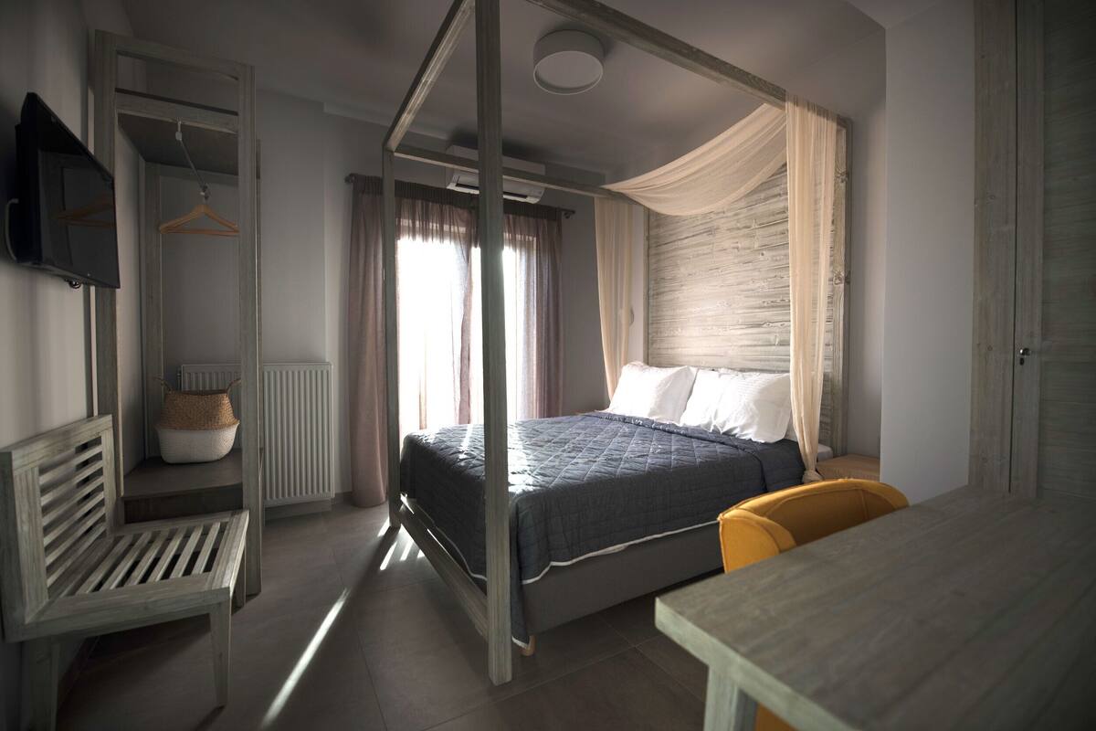 A bedroom with a four-poster bed, a wooden bench, a table, and a television mounted on the wall.